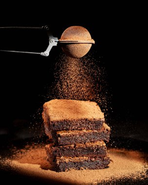 Siyah arka planda kakao tozlu çikolatalı kek.