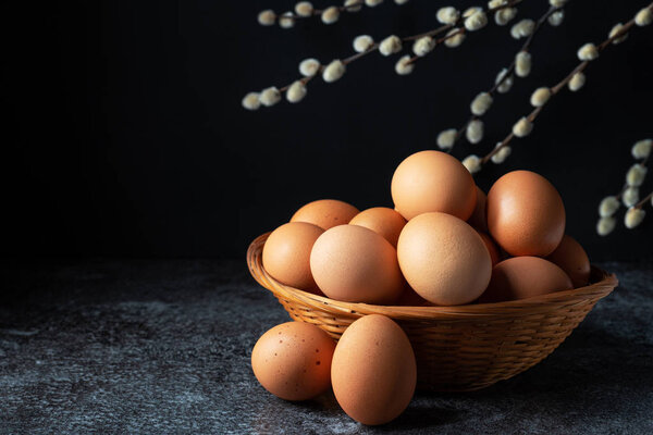 Chicken brown eggs in a wicker basket with pussy willow on a dark background