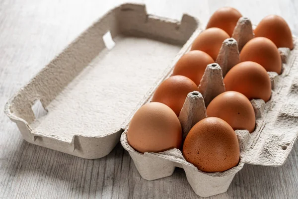 Chicken brown eggs in carton box on wooden background