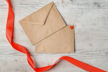 Kırmızı kalpli Kraft zarfları ve ahşap zemin üzerinde kırmızı saten kurdele Sevgililer Günü 'yle selamlaşmak için.