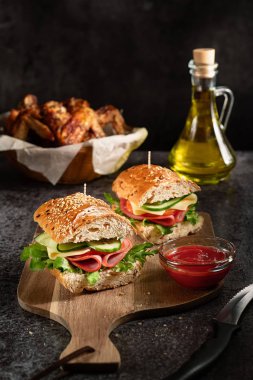 Köfteli sandviçler ve sebzeler ahşap kesme tahtasının üzerinde koyu arka planda. 