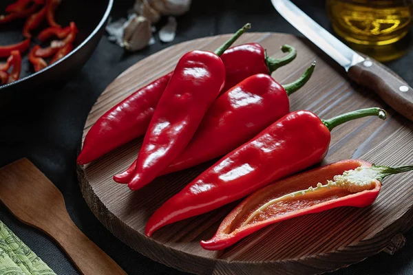 Siyah arka planda tahta bir kesme tahtasının üzerinde bıçaklı kırmızı biberler. Yemek hazırlıyorum. Yatay çekim