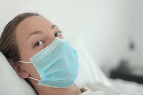 Girl feeling sick, lying in the bed wearing a face mask