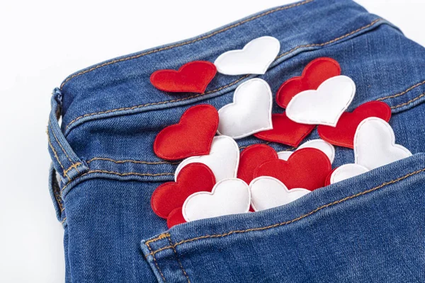 Set of fabric red and white hearts in blue jeans pocket on white background. Romantic surprise for valentines day. Denim texture background. Close up