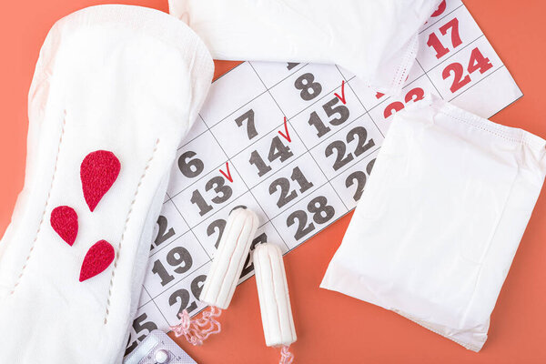 Protective menstrual pads, cotton tampons, contraceptive pills  and calendar of menstruation period on orange background. The concept of women gynecological health and intimate hygiene. Close up