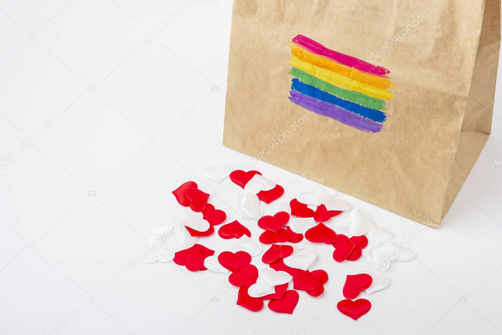 LGBT rainbow flag painted on a paper gift bag. Concept of LGBT and human rights. Many fabric hearts spilling out of the package. Gift for valentines day concept. Copy spase for text.
