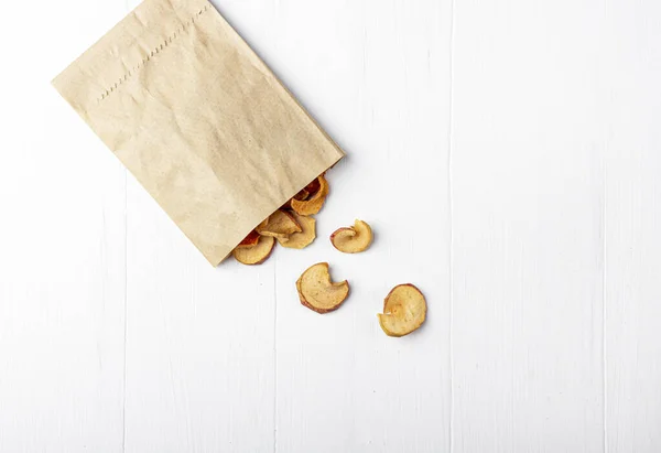 Organic homemade dry fruit chips in a paper eco pack on a white background. Healthy vegan snack of apples. The concept of proper nutrition,  organic and vegetarian food. Top view, copy space.