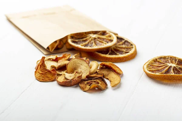 Organic homemade dry fruit chips in a paper eco pack on a white background. Healthy vegan snack of apples and orange. The concept of proper nutrition, organic and vegetarian food. Close up, copy space