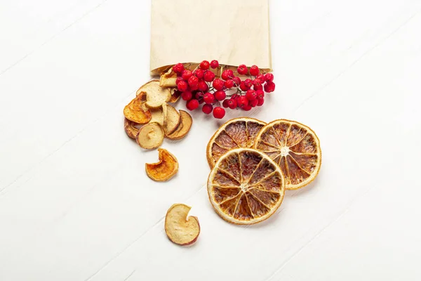 Organic homemade dry fruit chips in a paper eco pack on a white background. Healthy vegan snack of apples and orange. The concept of proper nutrition, organic and vegetarian food. Top view, copy space