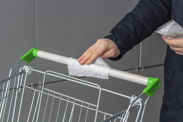Viral disease prevention concept. Man wipes down a handle of public shopping cart with a disinfecting moist towelette in mall or supermarket. Coronavirus prevention, safety rules during the epidemic