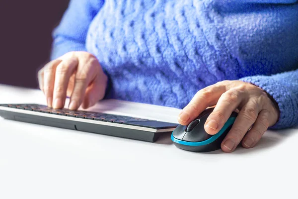 Elderly woman\'s hands typing on a PC keyboard close up. Pensioner working from home. The concept of learning seniors to computer literacy or internet skills. Selective focus.