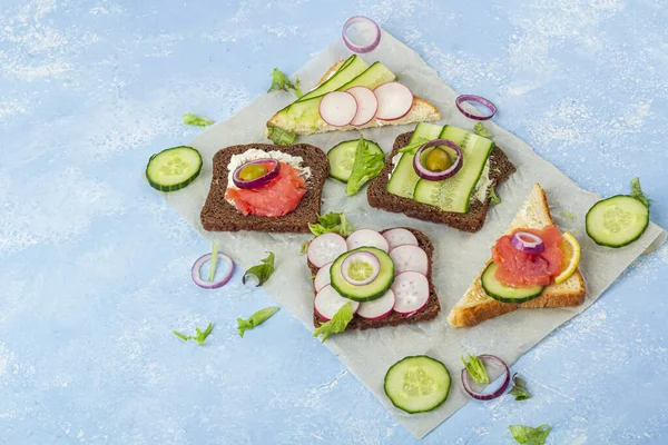 开胃菜 开胃三明治 配上不同的配料 鲑鱼和蔬菜放在蓝色背景的纸上 意大利或斯堪的纳维亚的传统小吃 健康饮食 复制文字空间 — 图库照片