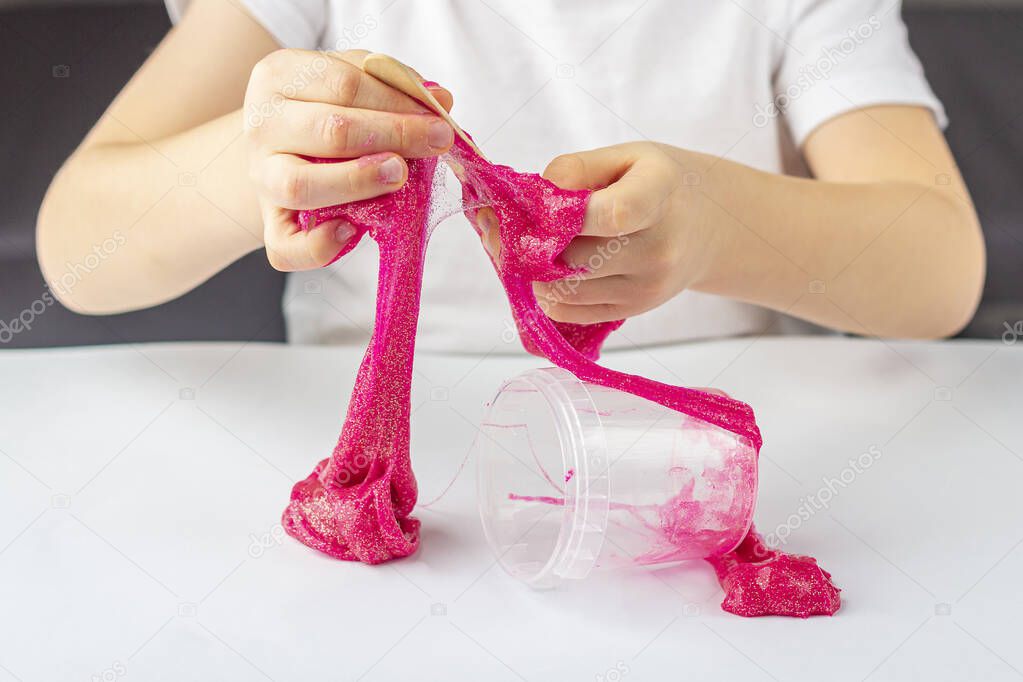 Step by step photo instruction: how to make slime at home. The concept of DIY.  Kids hands making pink slime toy. Step 9 get the finished slime from the container. Selective focus. 