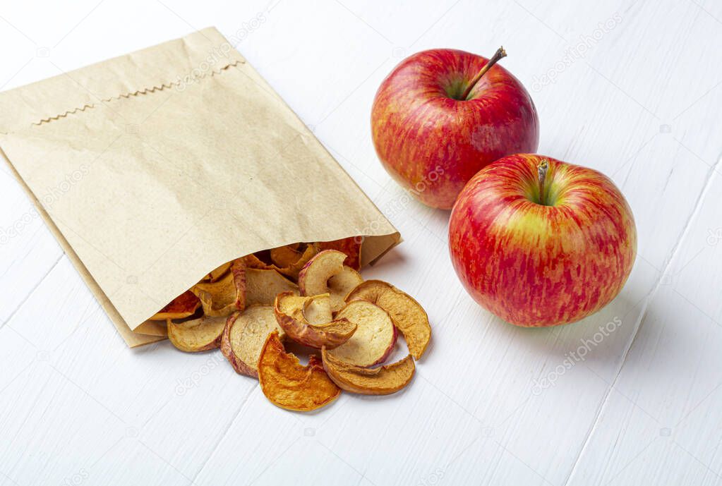 Organic homemade dry fruit chips in a paper eco pack and fresh apples on a white background. Healthy vegan snack of apples. The concept of proper nutrition, organic food. Close up, copy space