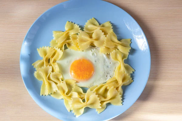 Child food. Funny food. Plate with pasta with fried egg in the form of funny face (sun). Children\'s menu and lunch concept. Flat lay, top view