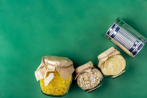 Food supplies during coronavirus quarantine and self-isolation. Food delivery, donation, volunteer support. Canned food, pasta and cereal on a green background. Copy space. Eco packaging, zero waste