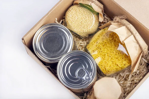 Food supplies during coronavirus quarantine and self-isolation. Food delivery, donation, volunteer support. Cardboard box with various canned food, pasta and cereal. Eco packaging. Copy space for text