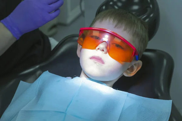 Child (little boy) in the dental chair with safety glasses, waiting for treatment. Kids dental medicine. Oral or dental examinations. Emotions of child in dental chair