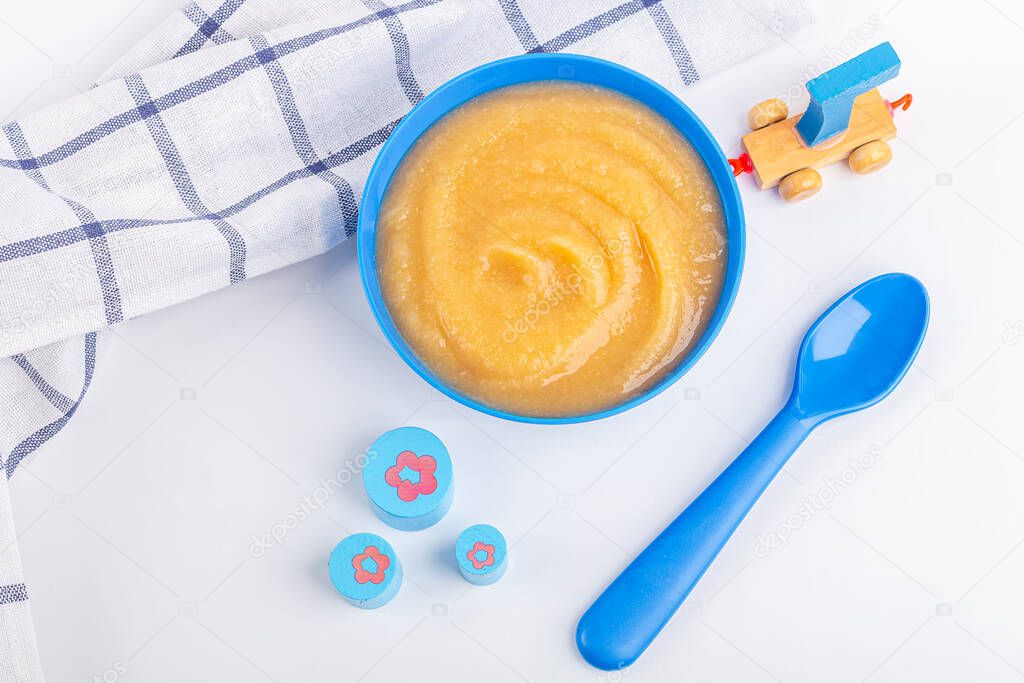 Baby food. Fresh homemade applesauce. Blue bowl with fruit puree on fabric and kids toys on table. The concept of proper nutrition and healthy eating. Organic and vegetarian food. Flat lay