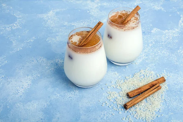 Homemade traditional mexican or spanish cool rice Horchata in a glass on blue background. Fresh cool drink or cocktail made from rice, vanilla and cinnamon or almond. Copy space for text