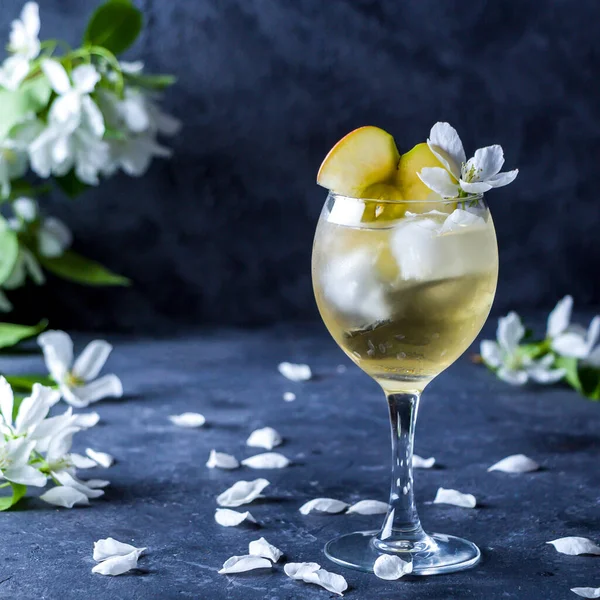 Apple cider or Calvados with ice cubes in wine glass. Refreshing cool summer drink, lemonade or ice tea decorated with apple tree petals. Copy space for text, low key