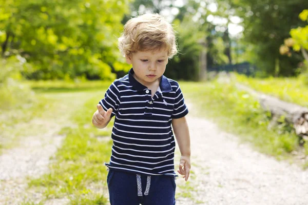 Ein kleiner Junge geht nach draußen. das Kind geht auf dem grünen Gras. — Stockfoto