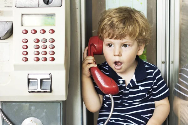 Bebis pratar på fast telefon. En pojke i en telefonkiosk. Röda telefonen — Stockfoto