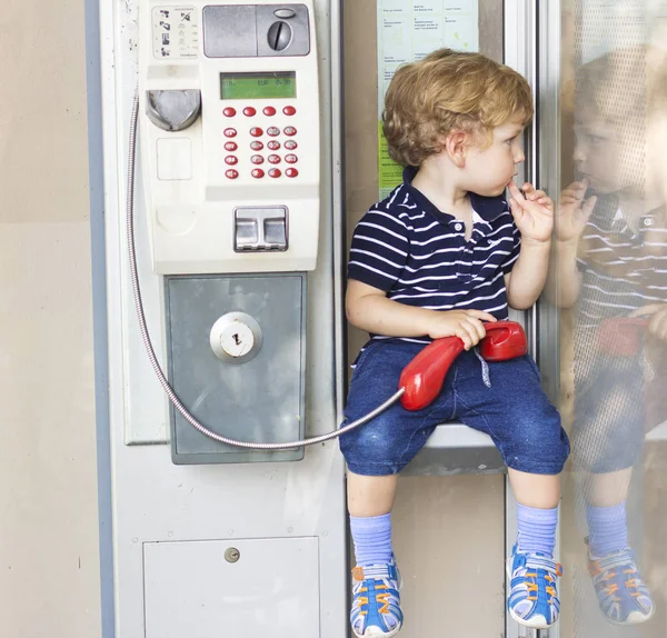 Bebé hablando por teléfono fijo. Un chico en una cabina telefónica. Auricular rojo — Foto de Stock