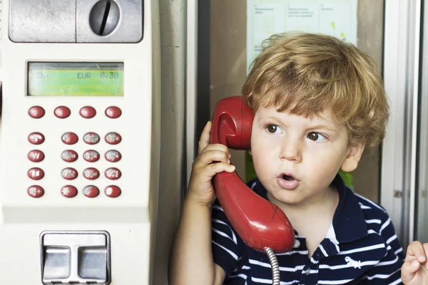 Dziecko rozmowa na telefon stacjonarny. Chłopiec w budce telefonicznej. Czerwoną słuchawkę — Zdjęcie stockowe