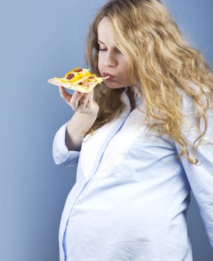 Hamile bir sarışın bir parça pizza yiyor. Gebelikte gıda