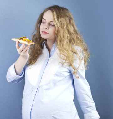 Hamile bir sarışın bir parça pizza yiyor. Gebelikte gıda