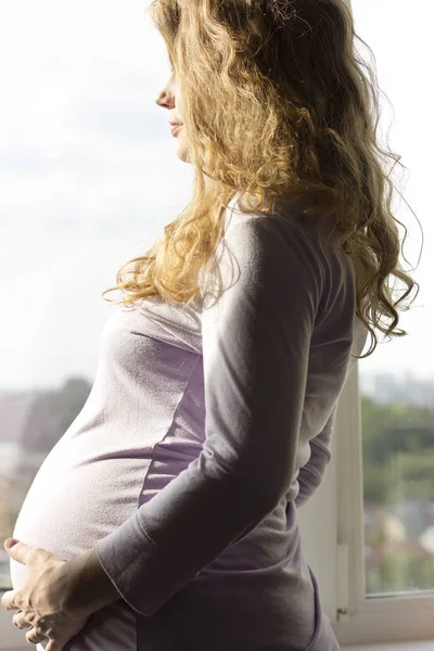 美丽的孕妇金发站附近的窗口和享受阳光 — 图库照片