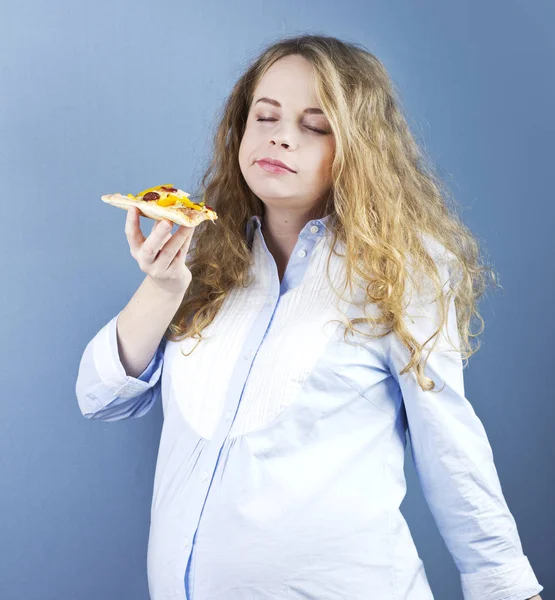 A pregnant blonde eats a piece of pizza. Food in Pregnancy