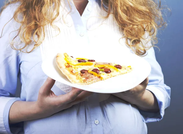 A pregnant blonde eats a piece of pizza. Food in Pregnancy
