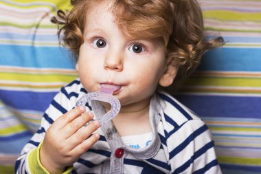 Bir çocuk lastik bir oyuncağı kemiriyor. Çocukların dişleri kesilmiş. İlk diş.