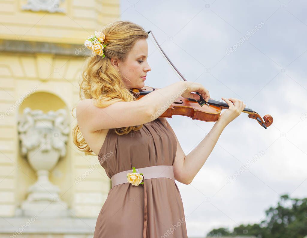 Beautiful smiling girl playing the violin outdoors. Curly blonde in a long dress. Girl playing the violin