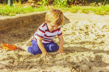 Kum havuzunda bir çocuk oynuyor. Bahçede küçük bir çocuk oynuyor..