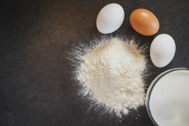 Pasta için gerekli malzemeler. Siyah arka planda yumurta, süt, un.. 