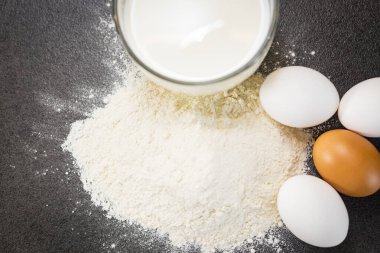 Siyah arka planda pişirmek için gerekli malzemeler. Hamur için gerekli malzemeler. Yumurta, süt, un..