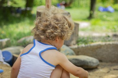 Kum havuzunda oynayan şirin bir çocuk. Küçük çocuk bahçede oynuyor.