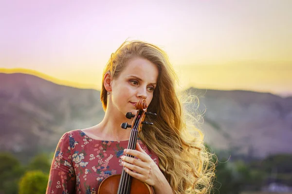 Woman with a violin in the rays of the setting sun. Portrait of a beautiful woman.