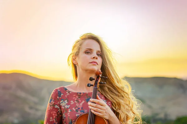 Woman with a violin in the rays of the setting sun. Portrait of a beautiful woman.