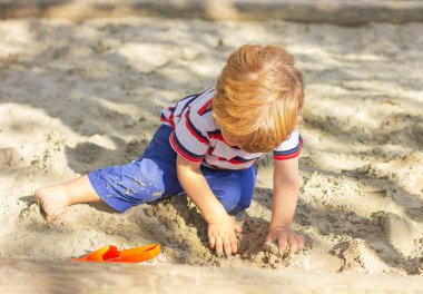 Kum havuzunda oynayan şirin bir çocuk. Küçük çocuk bahçede oynuyor.