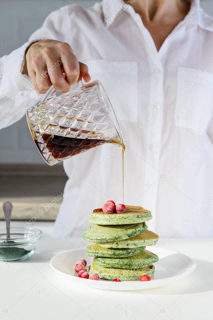 Spirulina pancakes stacked on a white plate. A man pours pancakes with maple syrup.