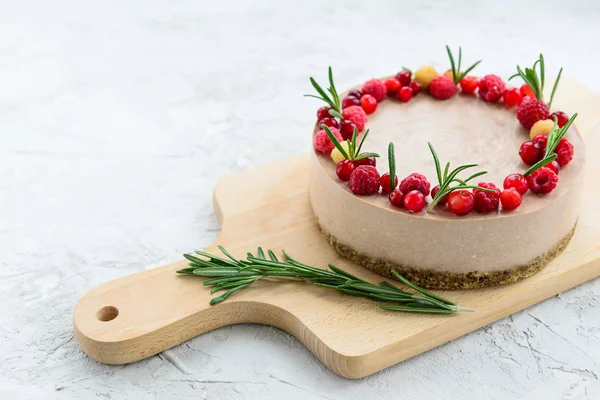 Raw cake decorated with raspberries and rosemary on a wooden board. Gluten free, vegetarian food. Horizontal orientation, copy space.