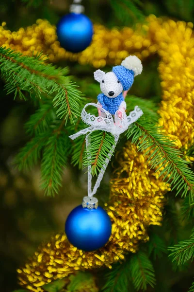 Knitted white mouse on a christmas tree decorated with blue christmas balls and tinsel. Symbol of the New Year 2020.