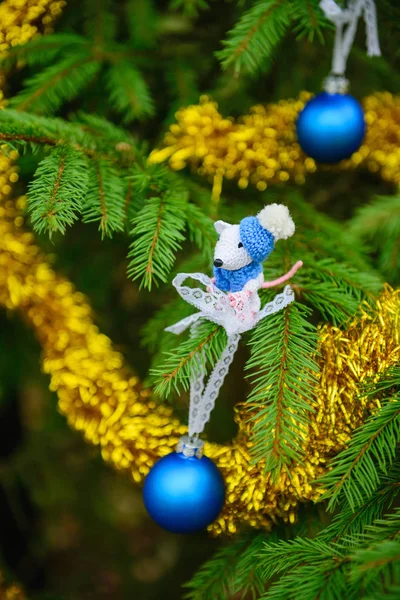 White mouse on a christmas tree decorated with blue christmas balls and tinsel. Symbol of the New Year 2020.