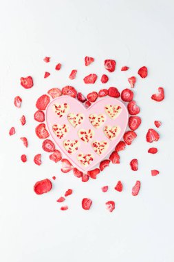 Beyaz çikolata ve beyaz bir masanın üzerindeki süblimleşmiş çileklerden yapılmış kalp şekeri. Sevgililer Günü.