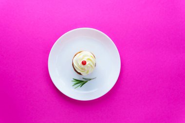 Krem peynirli kek, kızılcık ve pembe arka planda beyaz tabakta bir tutam biberiye..