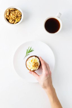 Kremalı havuçlu kek, ceviz, biberiye ve beyaz bir masada bir fincan kahve. Bir adam eliyle bir kek alır..